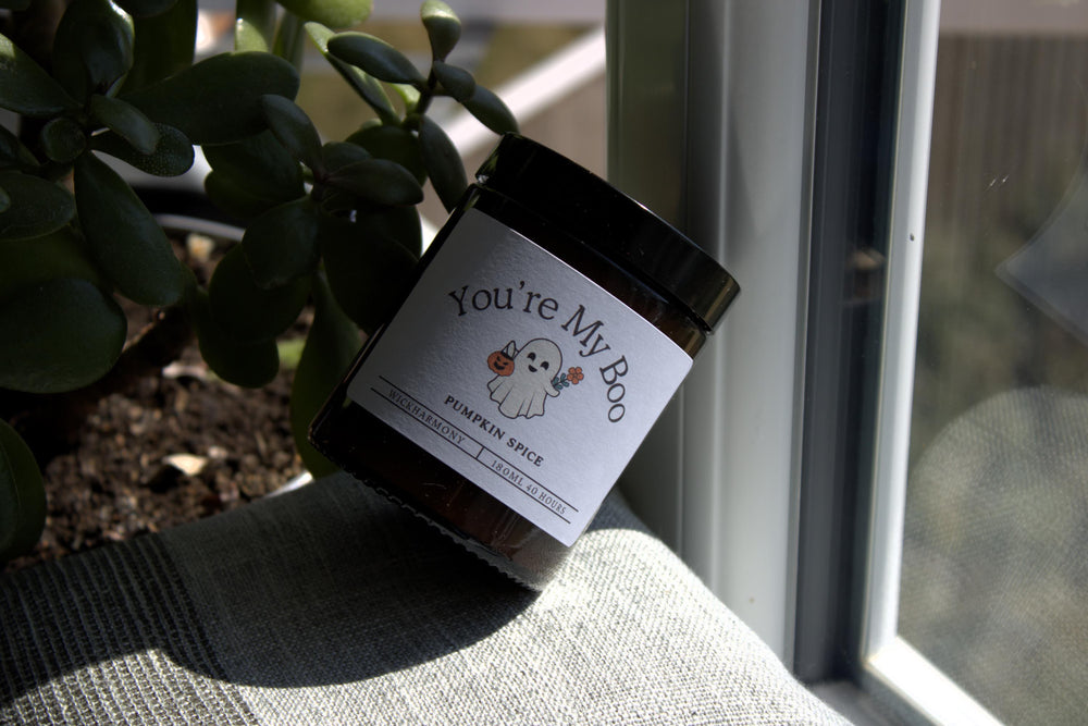 Jar of 'You're My Boo' pumpkin spice candle on a surface with plants in the background