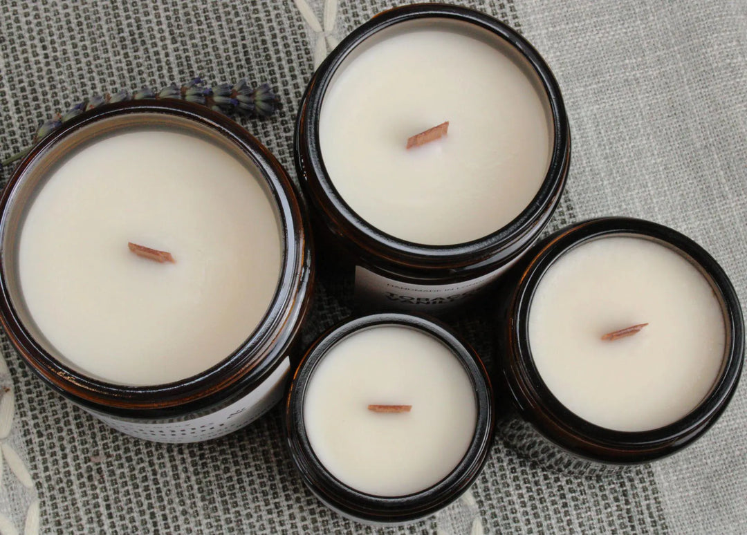 Four candles in glass jars with wooden wicks on a textured fabric background