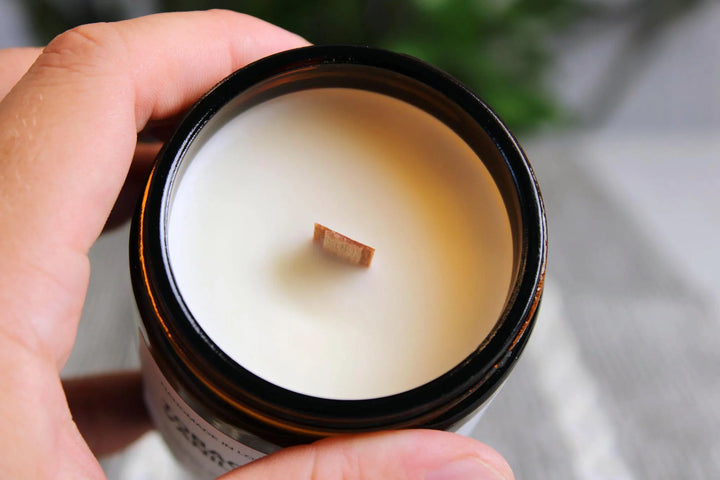 Hand holding a candle in an open container with a blurred background