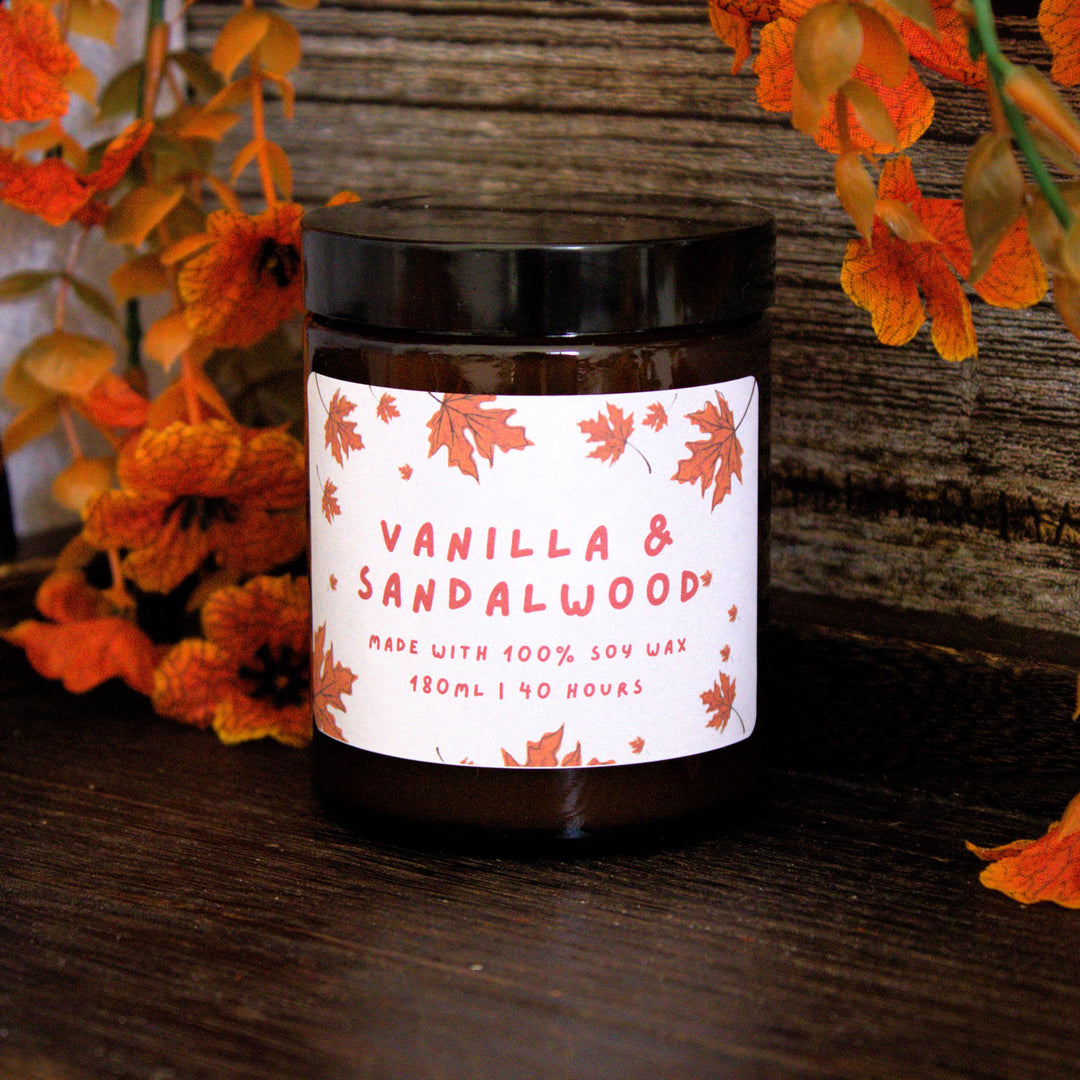 Candle jar labeled 'Vanilla & Sandalwood' with floral decorations on a wooden surface.
